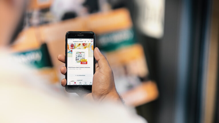 A person using the REWE app on a smartphone to view deals in the digital flyer. | © REWE digital, SEVN