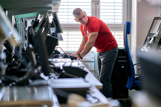Ein Mann in einem roten REWE digital T-Shirt arbeitet an einer Reihe von Computern in einem modernen Büro | © REWE digital