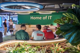 Sitzende und stehende Zuhörer:innen, die bei einer IT-Präsentation lachen