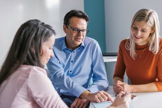 Drei Personen arbeiten gemeinsam an einem Tisch und besprechen Inhalte auf einem Tablet | © REWE digital, Paula Winkler und Alexander Gehring
