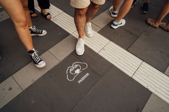 Feet of several people pointing to a floor sticker with the word "Passion" | © REWE digital, Paula Winkler & Alexander Gehring