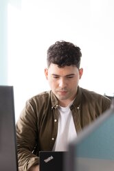 Ein junger Mann sitzt vor einem Computer und arbeitet konzentriert | © REWE digital