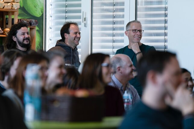 Diverse employees listening attentively to an internal IT-presentation | © REWE digital, hunderteins GmbH