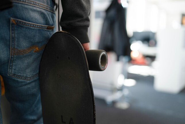 Symbolic image for work-life integration: an employee holding a skateboard in the office. | © REWE digital, Paula Winkler & Alexander Gehring