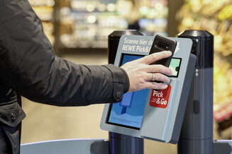 Eine Person scannt mit dem Smartphone einen Zugangspunkt von REWE Pick&Go in einem Markt. Das Bild zeigt den digitalen Zugang zu einem kassenlosen Einkaufserlebnis. | © REWE