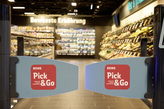Eingangsbereich eines REWE Pick&Go Markts mit geöffneten Zugangsschranken. Im Hintergrund sind Verkaufsregale und frische Lebensmittel zu sehen. Das Bild veranschaulicht das kassenlose Einkaufskonzept von REWE Pick&Go. | © REWE
