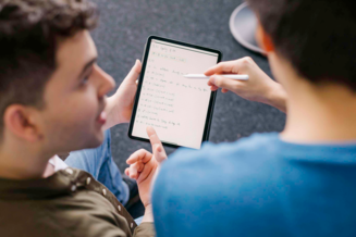 Zwei Personen betrachten gemeinsam ein Tablet mit handschriftlichen Notizen und digitalen Inhalten. Eine Person zeigt mit einem Stift auf den Bildschirm, während die andere auf Informationen verweist. | © REWE digital